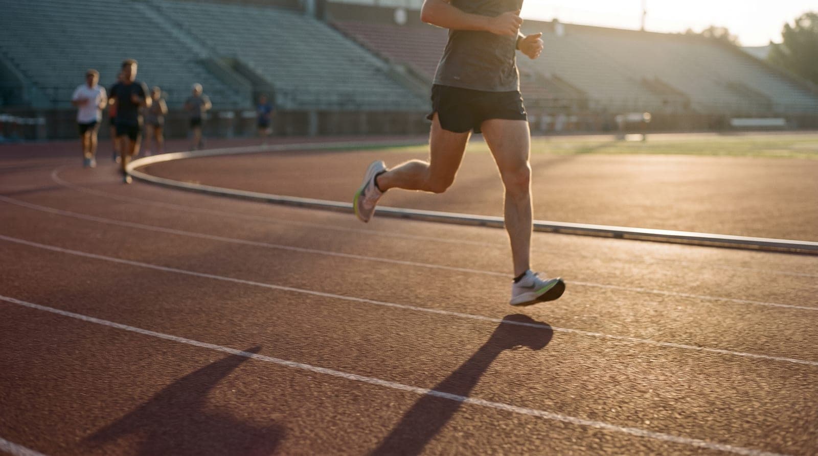 A runner mid-stride on an outdoor running track in early-morning light.
