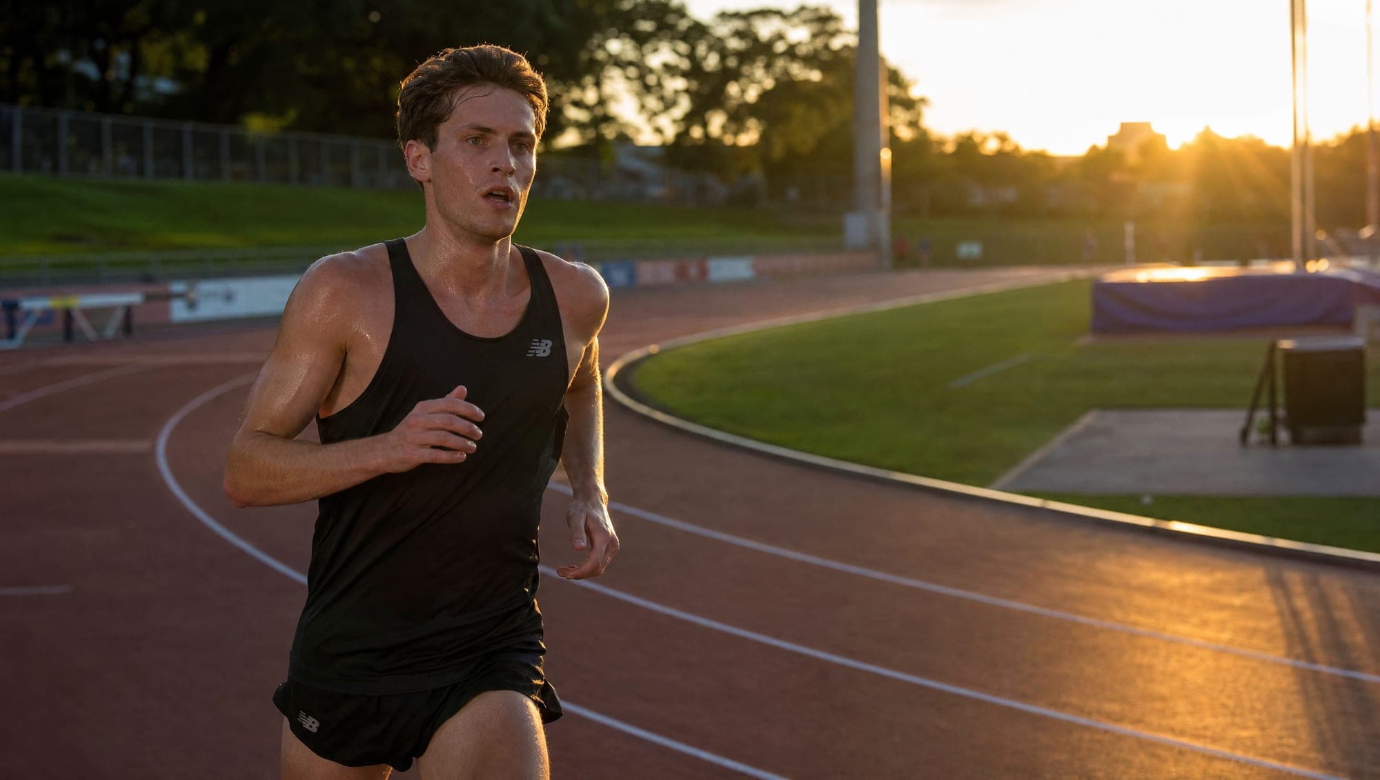A lone runner working hard mid-stride on an outdoor track in warm sunset light.